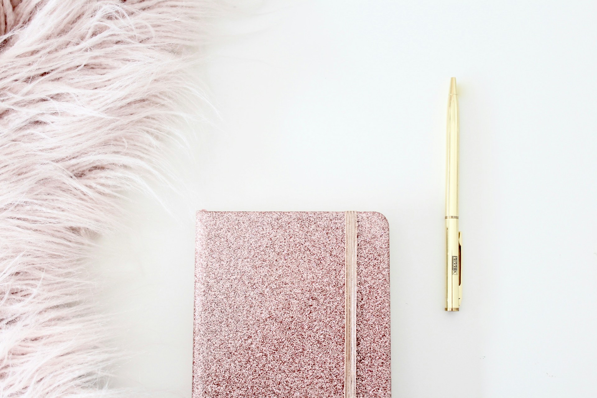 Image of a sparkly pink notebook with a gold pen laying next to it. 