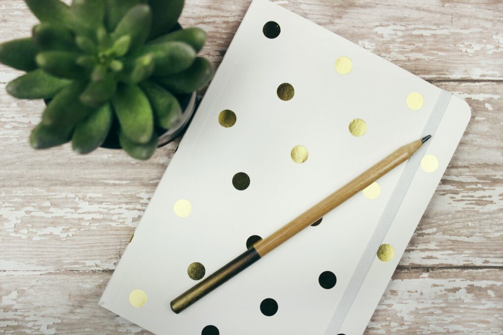 A poka dot journal laying on a wooden table with a gold pen resting on top. 